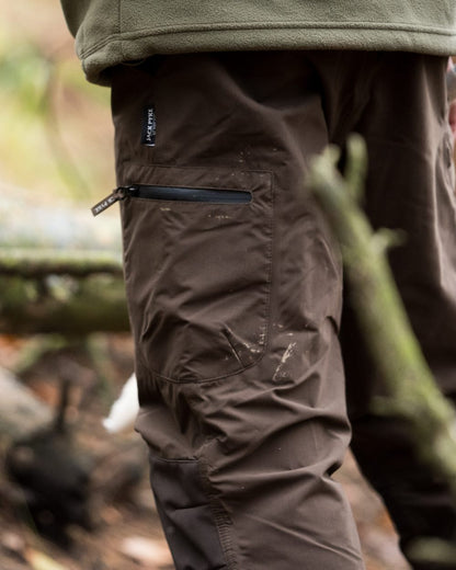 Brown coloured Jack Pyke Weardale Hunting Trousers on forest background #colour_brown
