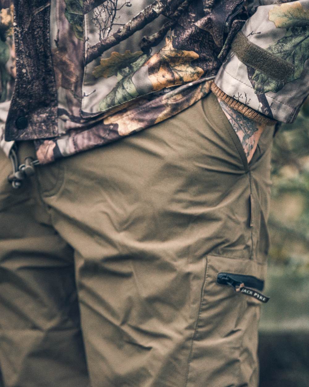 Green coloured Jack Pyke Weardale Hunting Trousers on forest background #colour_green