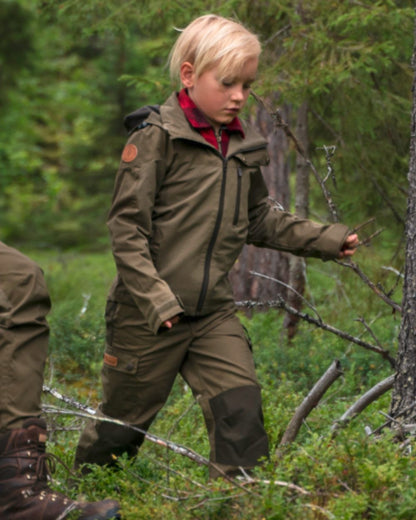 Hunting Olive coloured Pinewood Childrens Finnveden Hybrid Jacket on forest background #colour_hunting-olive