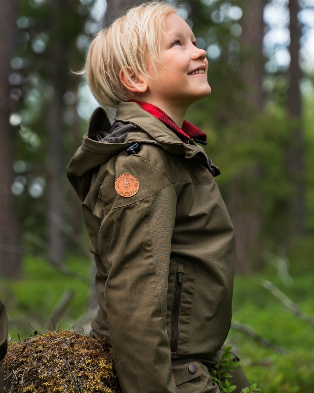 Hunting Olive coloured Pinewood Childrens Finnveden Hybrid Jacket on forest background #colour_hunting-olive
