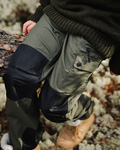 Mid Green Black coloured Pinewood Childrens Lappland Trousers on forest background #colour_mid-green-black