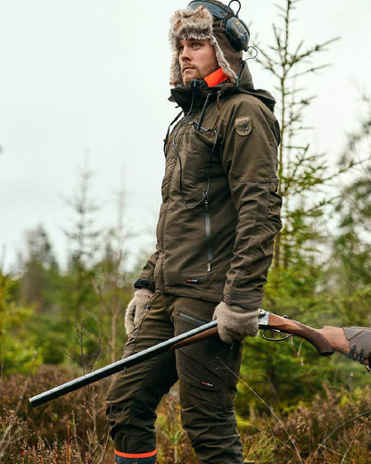 Moss Green coloured Pinewood Mens Hunter Pro Extreme 2.0 Trousers on forest background #colour_moss-green