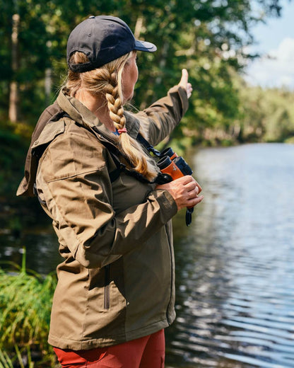 Hunting Olive Coloured Pinewood Womens Finnveden Hybrid Jacket on forest background #colour_hunting-olive