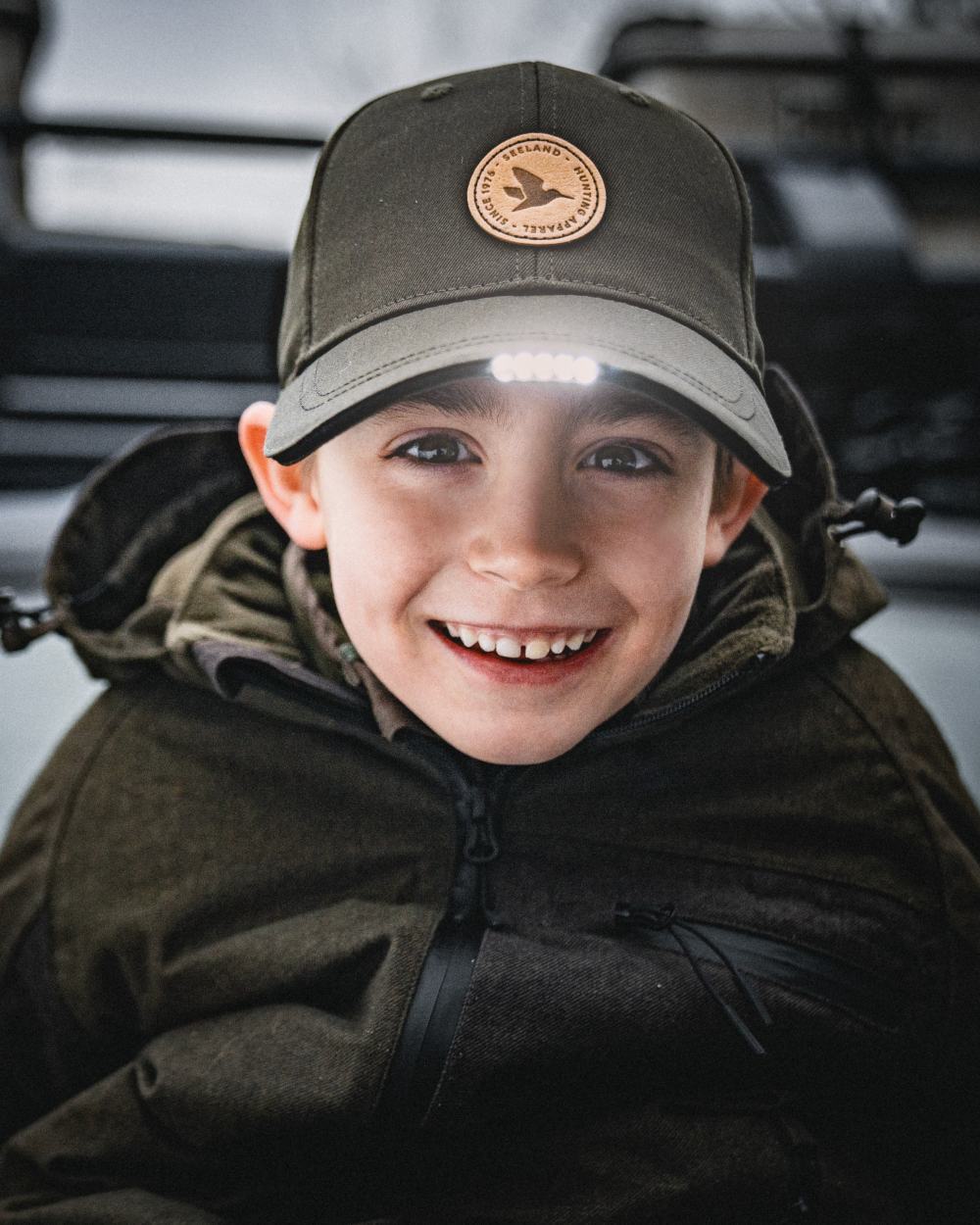 Pine Green coloured Seeland Childrens Skarn LED Junior Cap on forest background #colour_pine-green