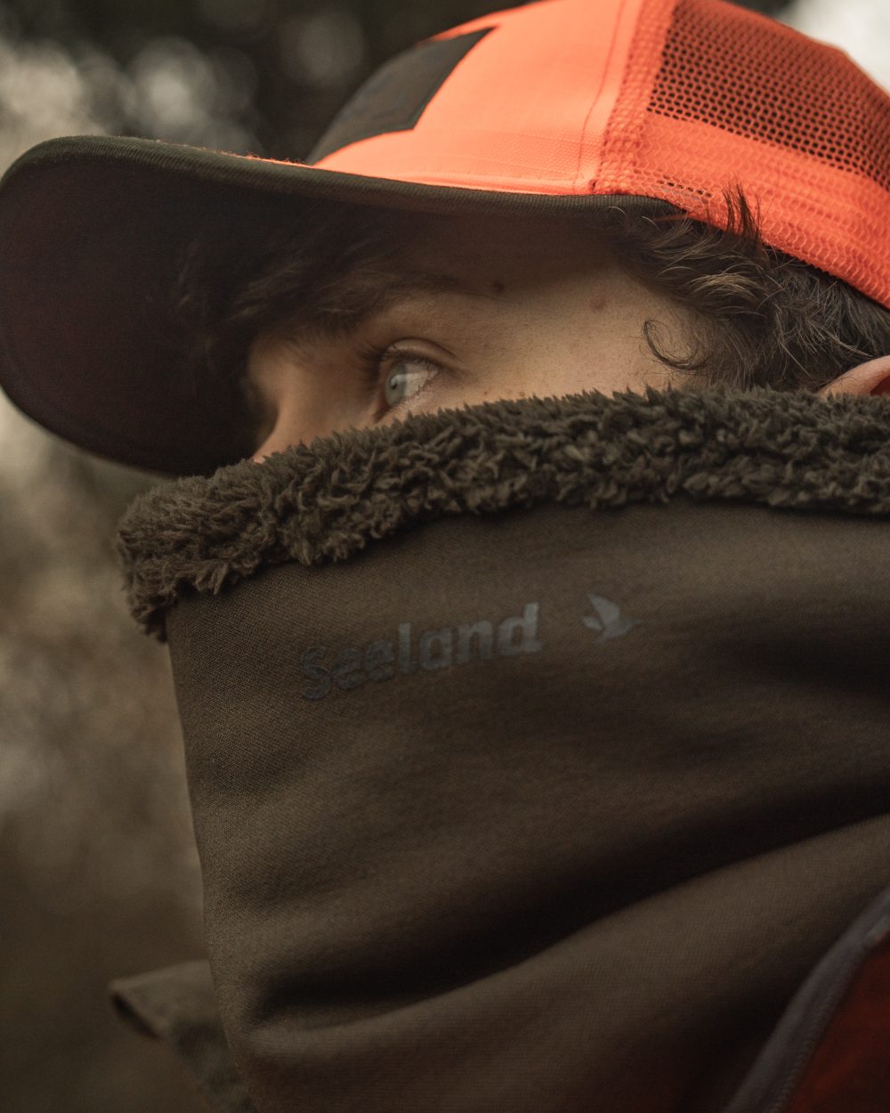 Pine Green coloured Seeland Iron Neckgaiter on forest background #colour_pine-green