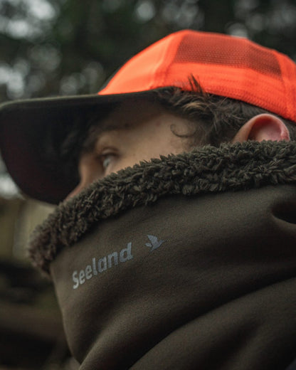 Pine Green coloured Seeland Iron Neckgaiter on forest background #colour_pine-green