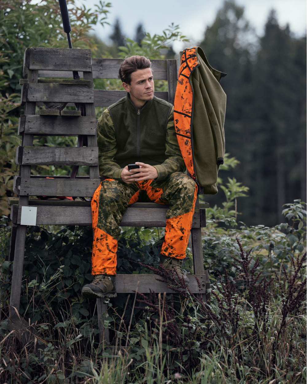 InVis Green InVis Orange Blaze Coloured Seeland Vantage Trousers on forest background #colour_invis-green-invis-orange-blaze