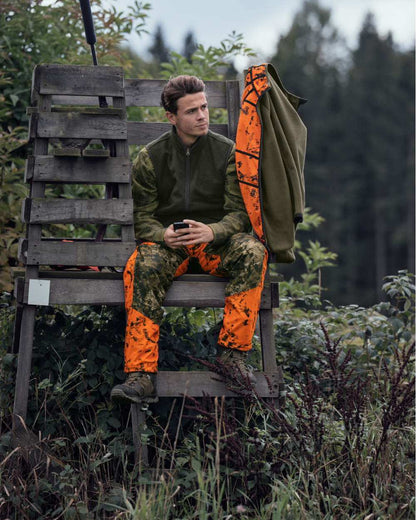InVis Green InVis Orange Blaze Coloured Seeland Vantage Trousers on forest background #colour_invis-green-invis-orange-blaze