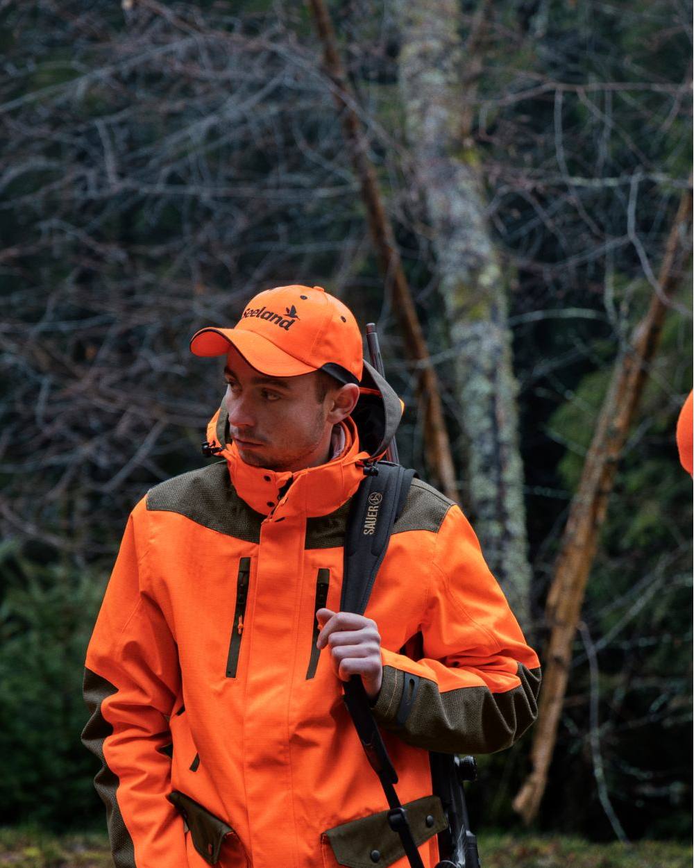 Pine Green Hi-Vis Orange Coloured Seeland Venture Rover Jacket on forest background #colour_pine-green-hi-vis-orange