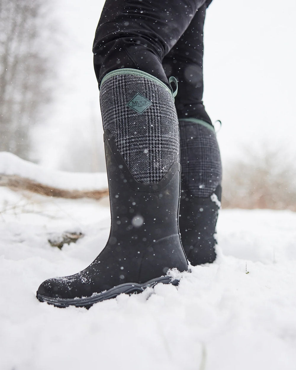 Black Plaid Print Muck Boots Womens Artic Sport II Tall Wellingtons on Snowy background #colour_plaid-print