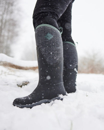 Black Plaid Print Muck Boots Womens Artic Sport II Tall Wellingtons on Snowy background #colour_plaid-print